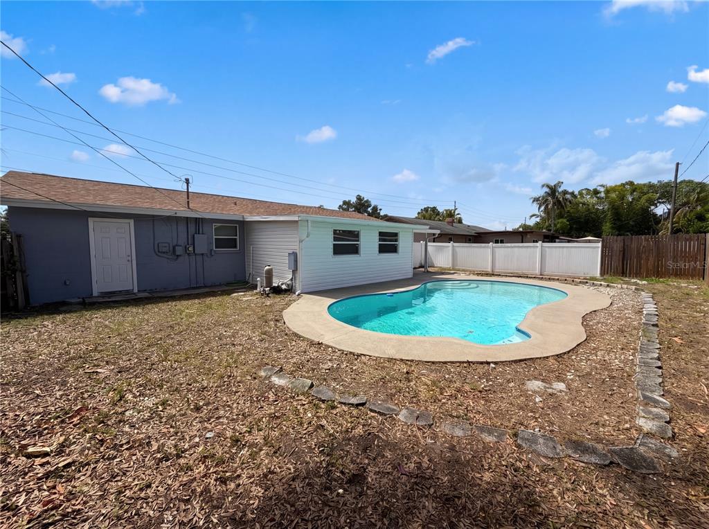 A backyard features a swimming pool, a white vinyl fence, and the rear of a house — 15525 BEDFORD CIRCLE E, CLEARWATER, FL