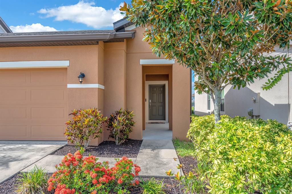 The exterior of a tan house features a garage, a recessed front door, and landscaping — 5148 BRICKWOOD RISE DRIVE, WIMAUMA, FL