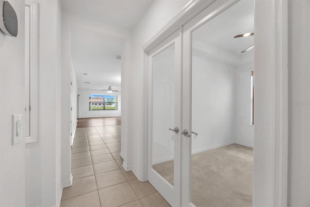 A hallway with tile flooring leads to a room with French doors and carpet — 5148 BRICKWOOD RISE DRIVE, WIMAUMA, FL
