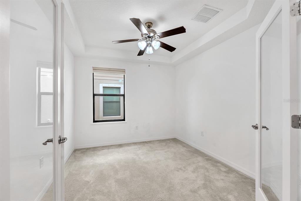 A small, empty room with white walls, carpeted flooring, a ceiling fan, and French doors — 5148 BRICKWOOD RISE DRIVE, WIMAUMA, FL
