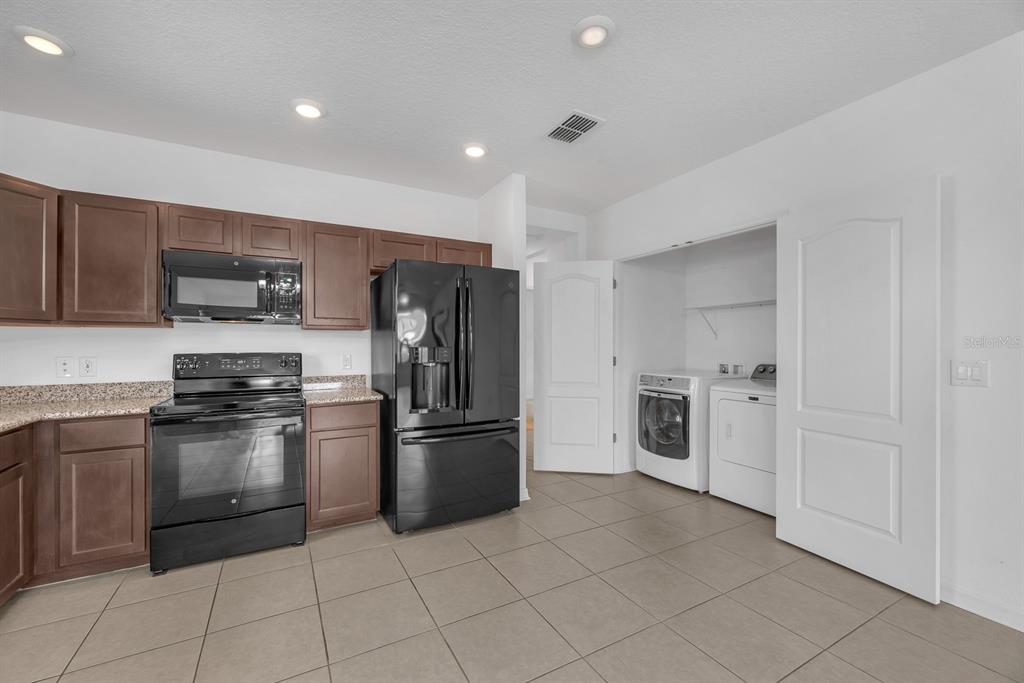 A kitchen with brown cabinets, black appliances, and an adjacent laundry closet with white doors — 5148 BRICKWOOD RISE DRIVE, WIMAUMA, FL