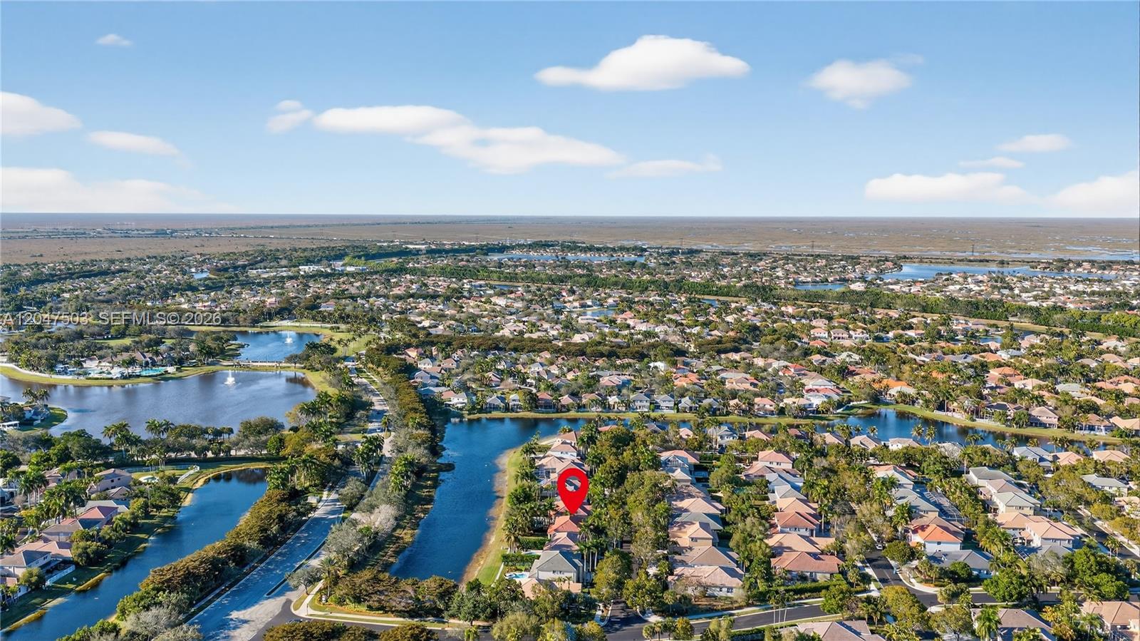 An aerial view shows a residential neighborhood with houses surrounding a lake and canal — 1325 Chenille Cir, Weston FL 33327, WESTON, FL