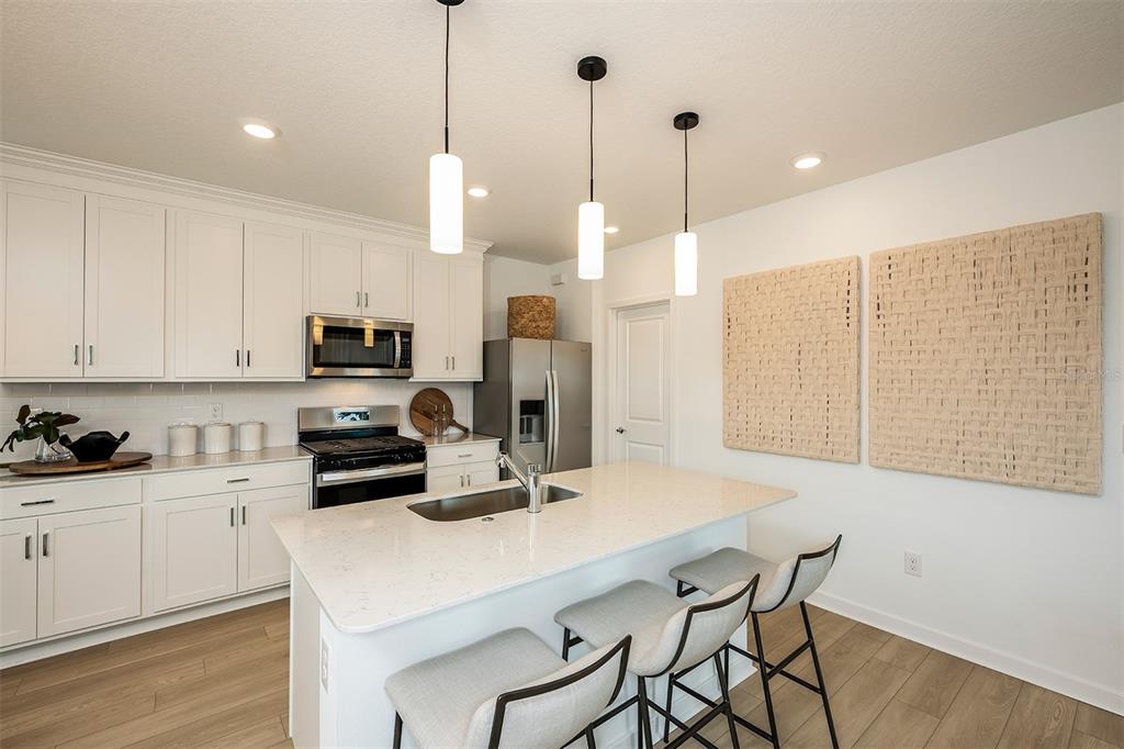 A modern kitchen features white cabinetry, a quartz island with bar seating, and pendant lighting — 6279 BROAD FIELD AVENUE, APOLLO BEACH, FL