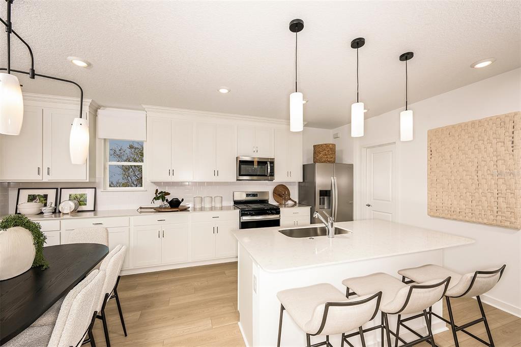 A bright kitchen features white cabinetry, a central island with bar seating, and pendant lighting — 6279 BROAD FIELD AVENUE, APOLLO BEACH, FL