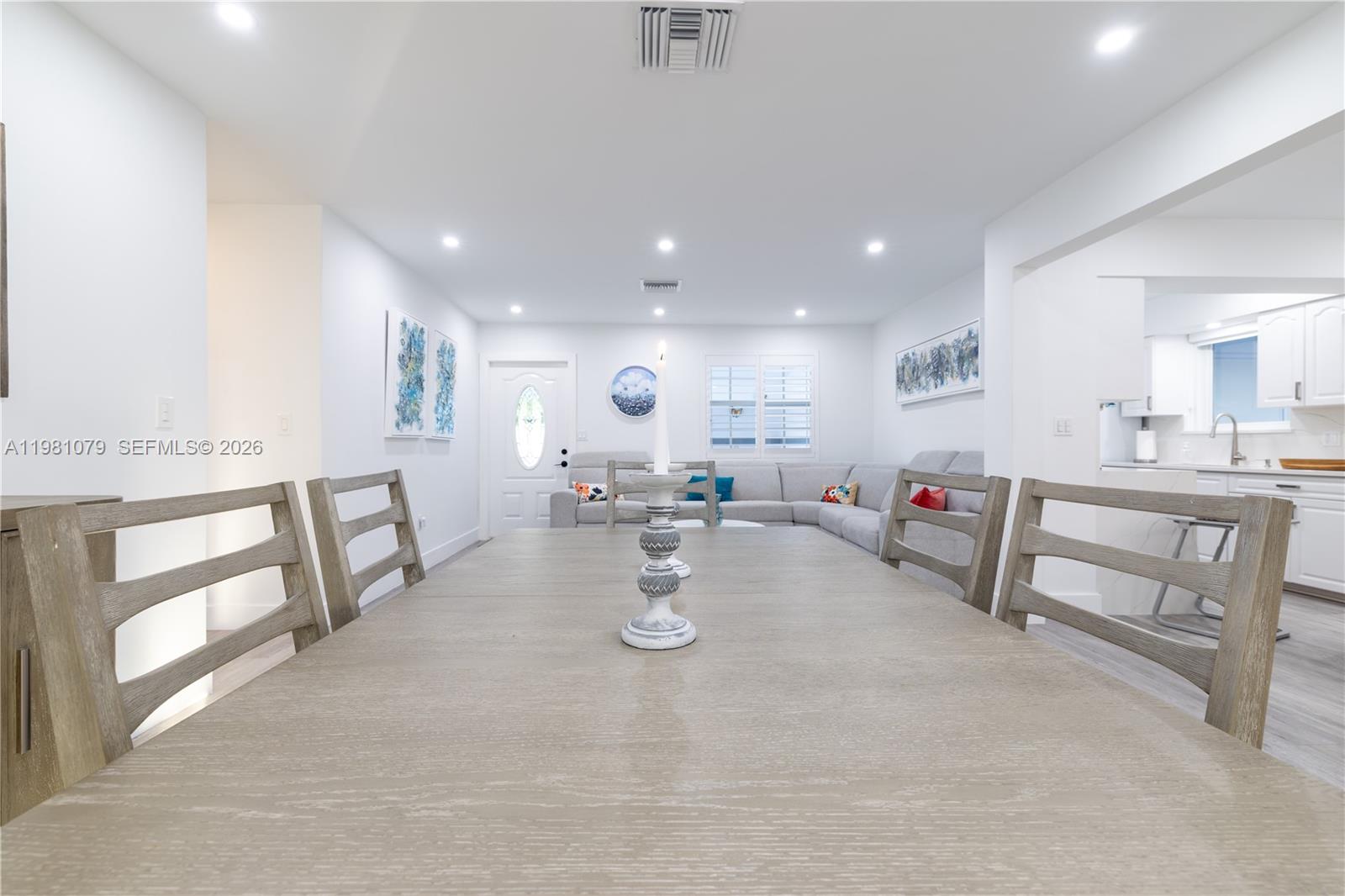 A dining area with a wooden table leads into a living room and kitchen — 19600 Gulfstream Rd, Cutler Bay FL 33157, CUTLER BAY, FL