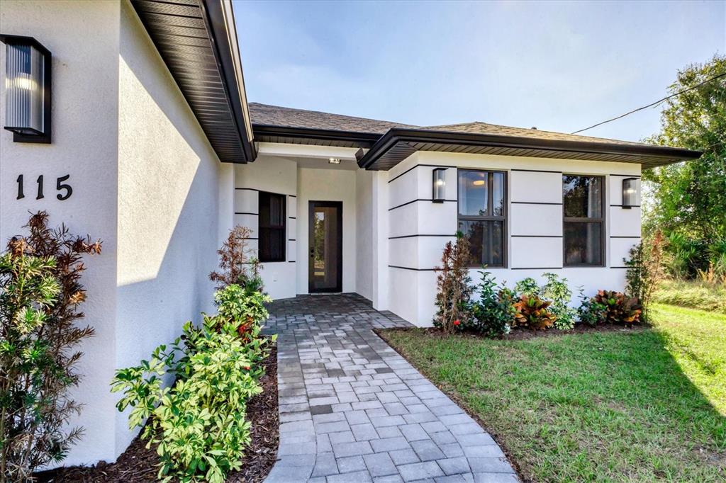 The exterior of a modern white house features a paved walkway leading to the front door — 115 GREEN PINE PARK, ROTONDA WEST, FL