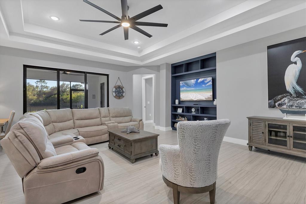 A living room features a sectional sofa, a patterned armchair, and a blue built-in media center — 115 GREEN PINE PARK, ROTONDA WEST, FL