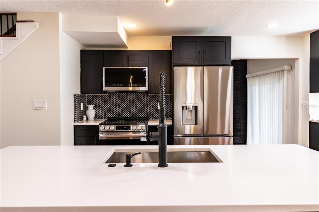 A modern kitchen features black cabinets, stainless steel appliances, a herringbone backsplash, and a white island — 226 WILLOWICK AVENUE, TEMPLE TERRACE, FL