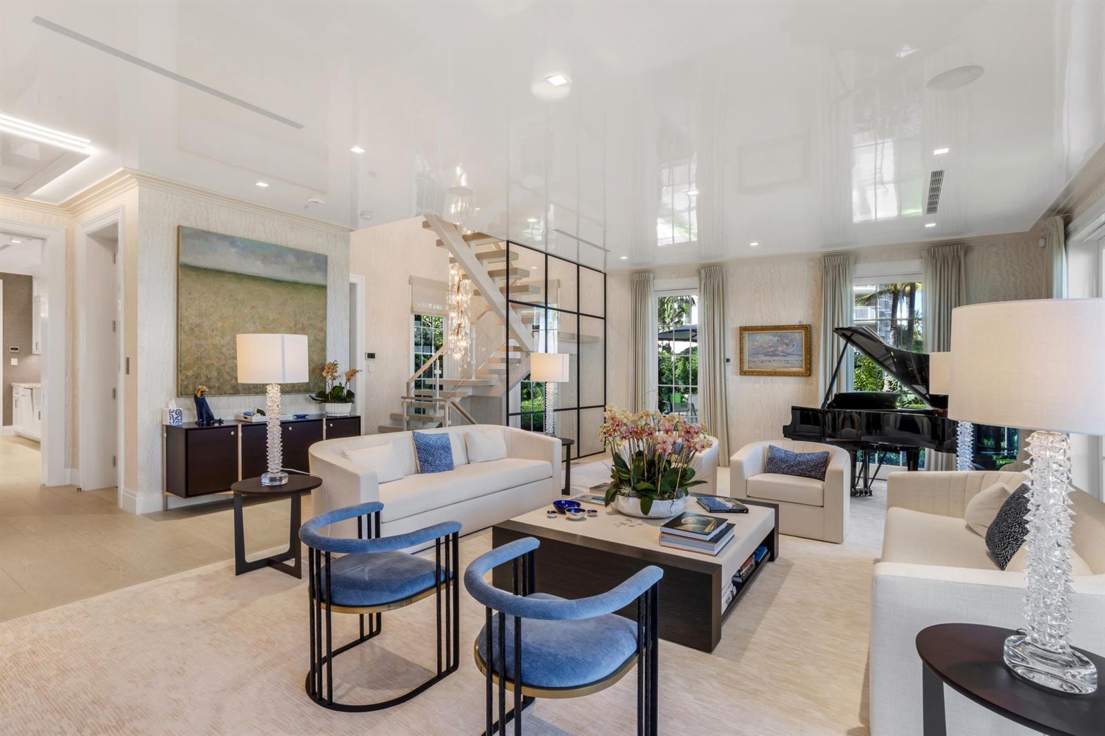 A bright living room features a grand piano, a staircase, and modern blue accent chairs — 456 S Ocean Boulevard, Palm Beach FL 33480, PALM BEACH, FL