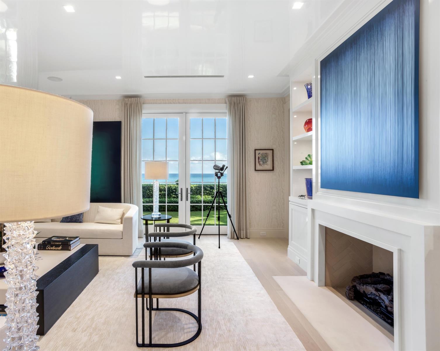 A bright living room features a fireplace, modern armchairs, and a view of the ocean — 456 S Ocean Boulevard, Palm Beach FL 33480, PALM BEACH, FL