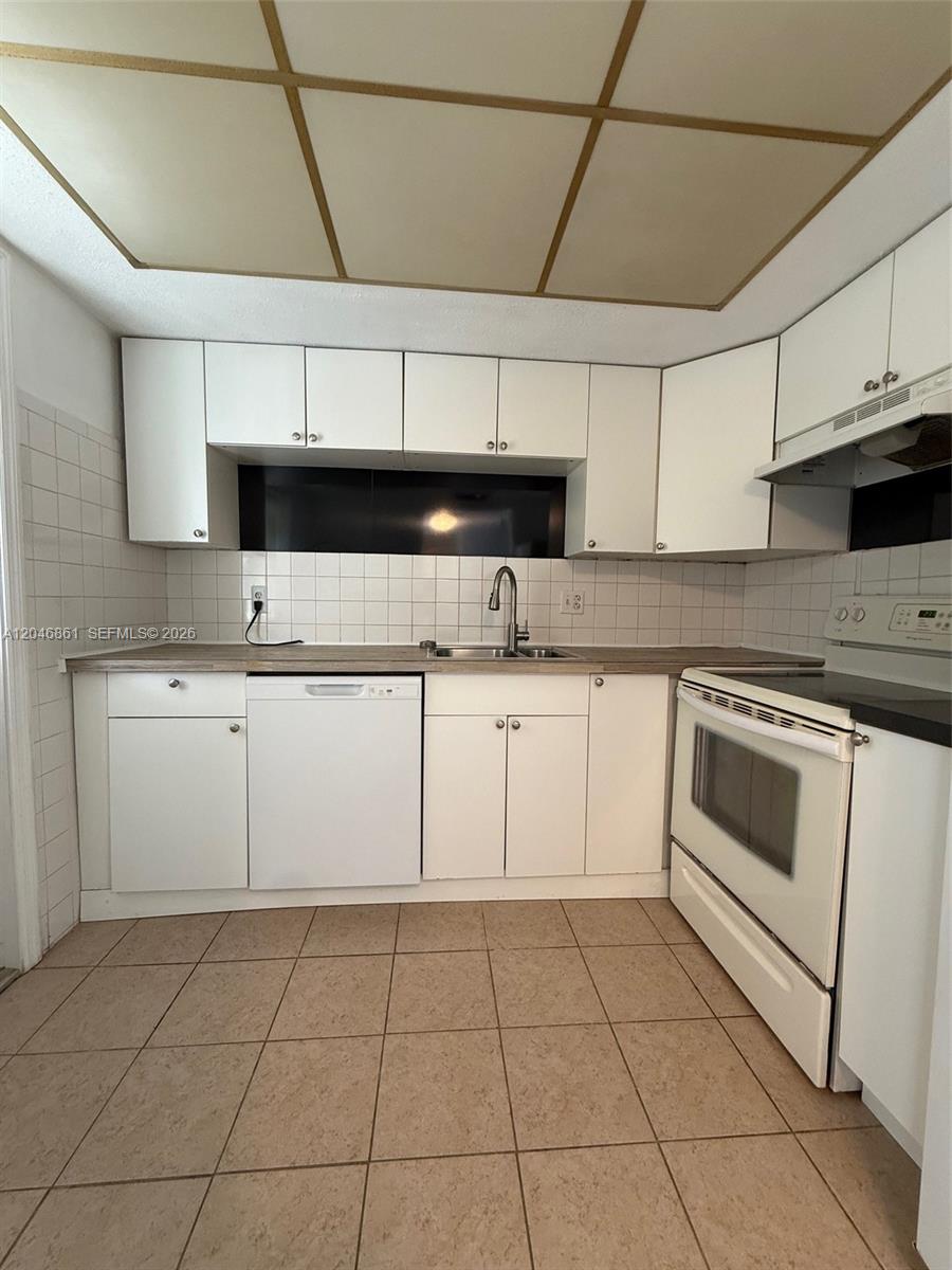 A kitchen features white cabinets, a dishwasher, a stove, and tiled floors and walls — 3300 NE 10th Ter # 53, Pompano Beach FL 33064, POMPANO BEACH, FL