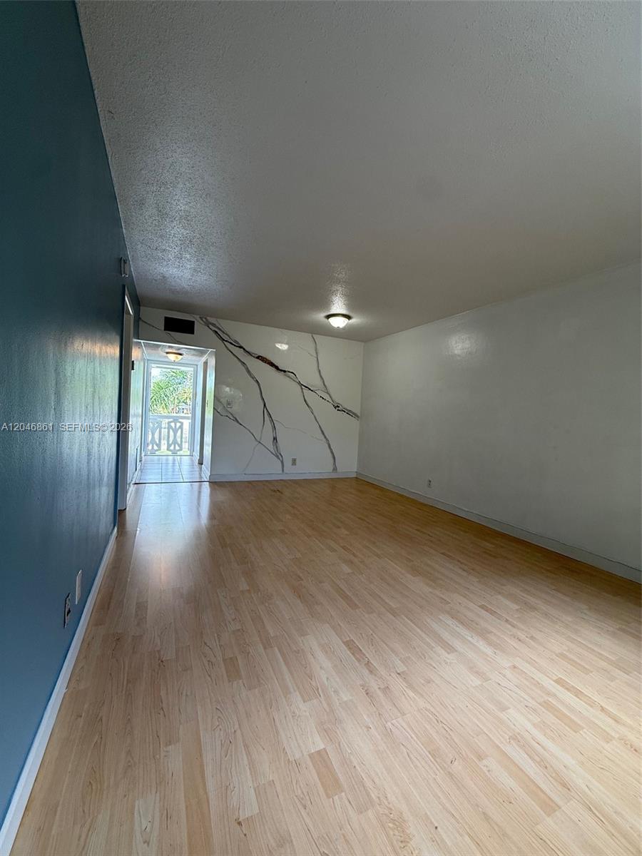 An empty room with light wood floors, a blue wall, and a marble-patterned accent wall — 3300 NE 10th Ter # 53, Pompano Beach FL 33064, POMPANO BEACH, FL