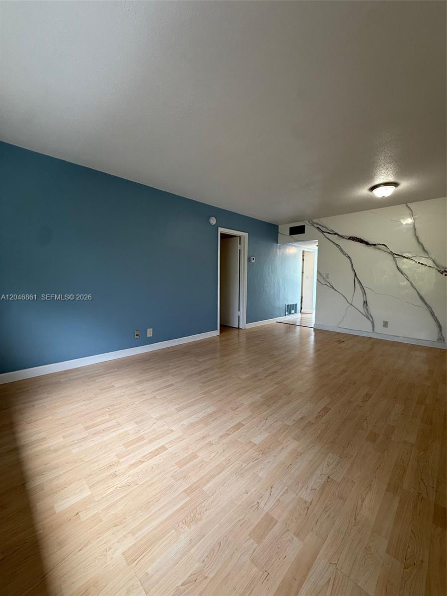 An empty room features light wood-look flooring, a blue accent wall, and a marble-patterned wall — 3300 NE 10th Ter # 53, Pompano Beach FL 33064, POMPANO BEACH, FL
