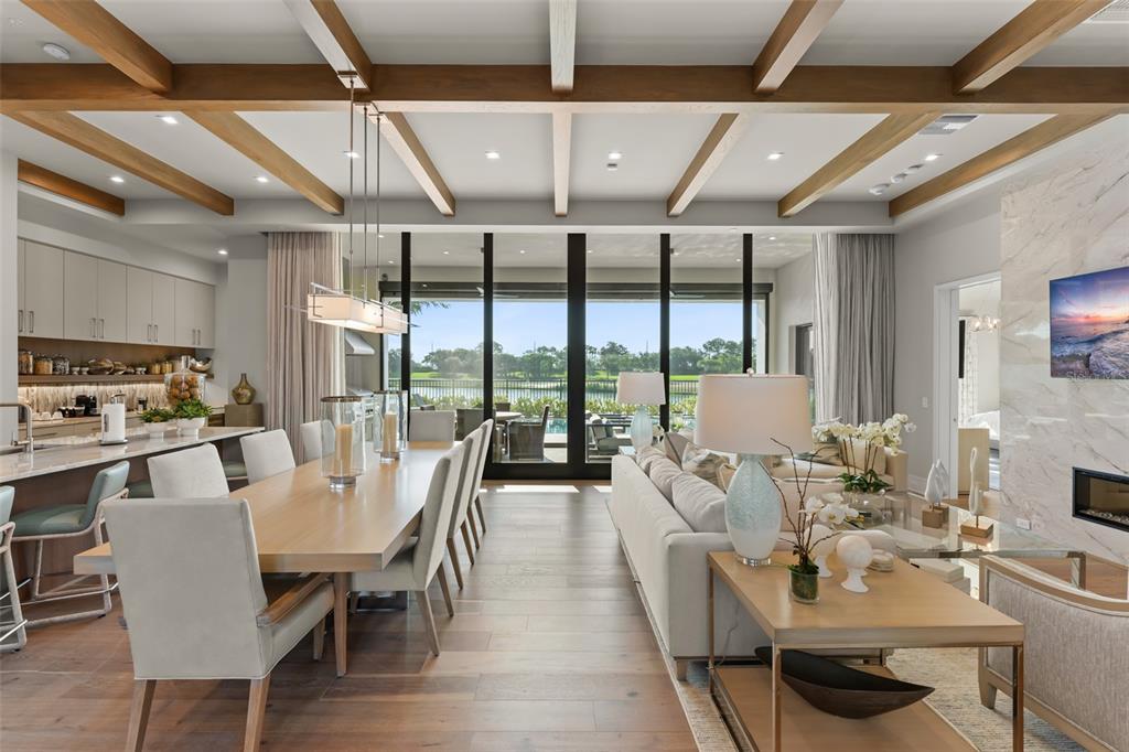 An open-concept living and dining area features wood-beamed ceilings, light flooring, and large glass doors — 4018 GRANDE BRICK LOOP, ORLANDO, FL