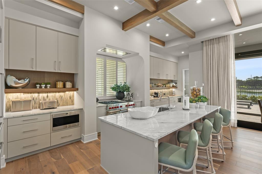 A modern kitchen features a marble-topped island, light cabinetry, wood beams, and a view outdoors — 4018 GRANDE BRICK LOOP, ORLANDO, FL