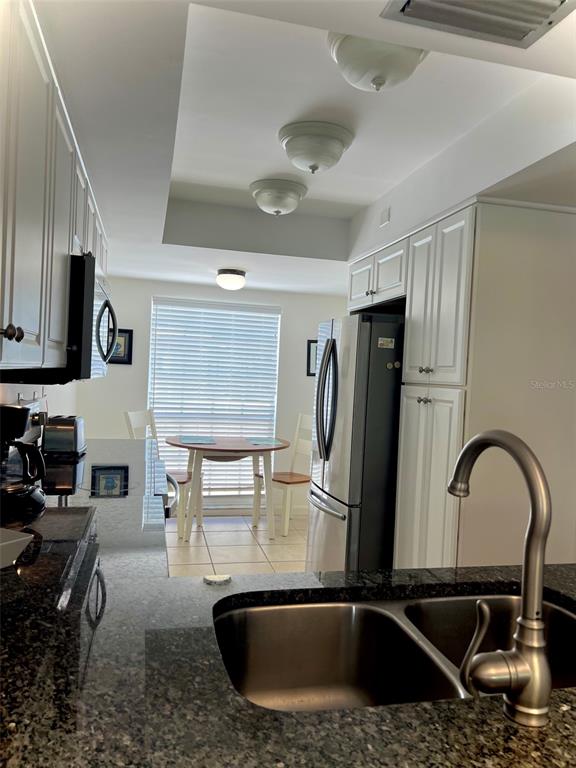 A kitchen features dark granite countertops, white cabinetry, stainless steel appliances, and a dining area — 5242 WEDGEWOOD LANE UNIT 62, SARASOTA, FL