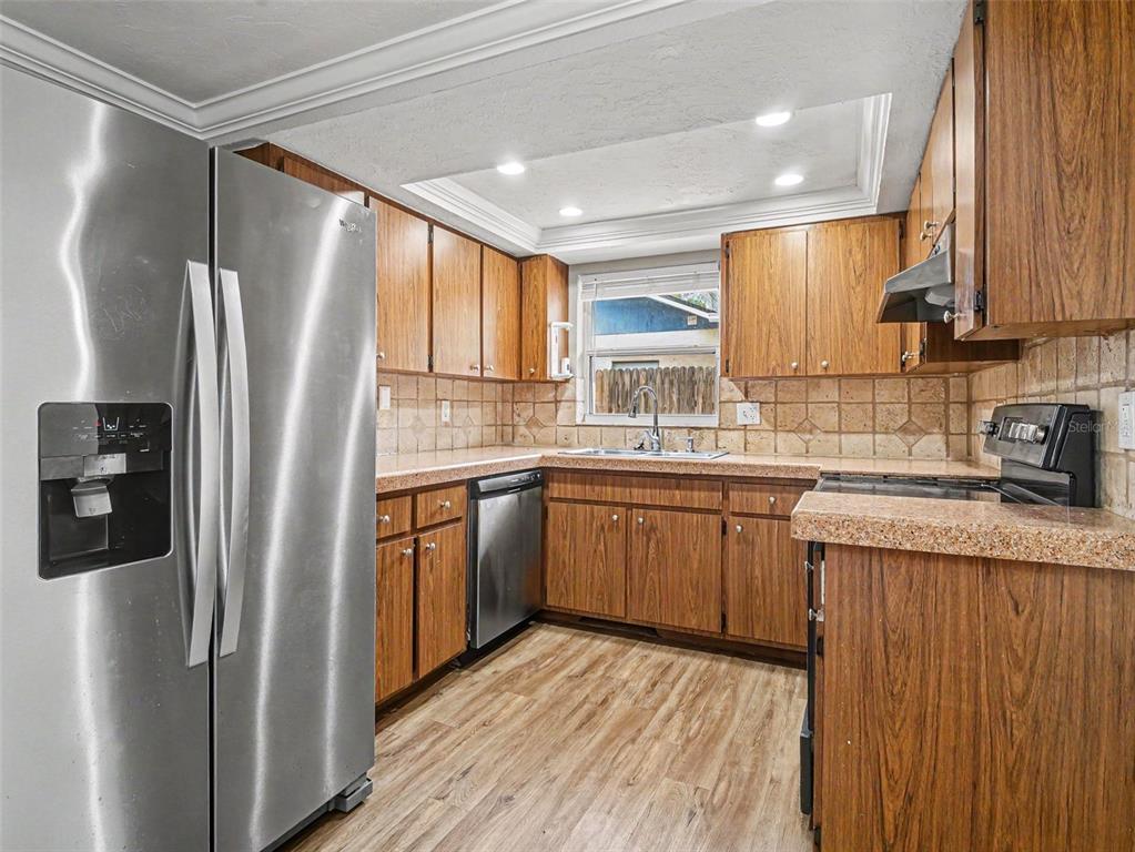 A kitchen features wood cabinets, stainless steel appliances, a tiled backsplash, and wood-look flooring — 2111 FAIRFIELD AVENUE, SARASOTA, FL