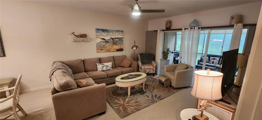 A living room features a sectional sofa, patterned rug, coffee table, and sliding glass doors — 9600 FIDDLERS GREEN CIRCLE UNIT 110, ROTONDA WEST, FL