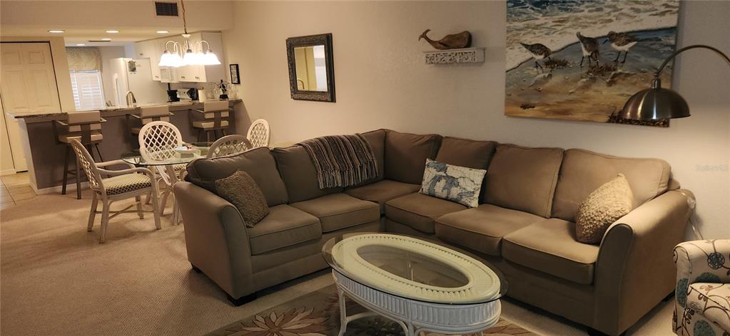 A living room with a sectional sofa and coffee table opens to a kitchen area — 9600 FIDDLERS GREEN CIRCLE UNIT 110, ROTONDA WEST, FL