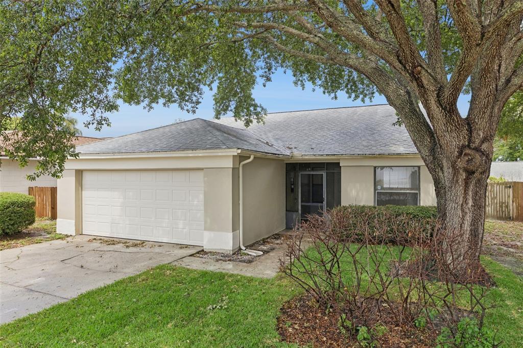 A single-story house with a white garage door, beige stucco exterior, and a large oak tree — 1008 OLLIFF WAY, OVIEDO, FL