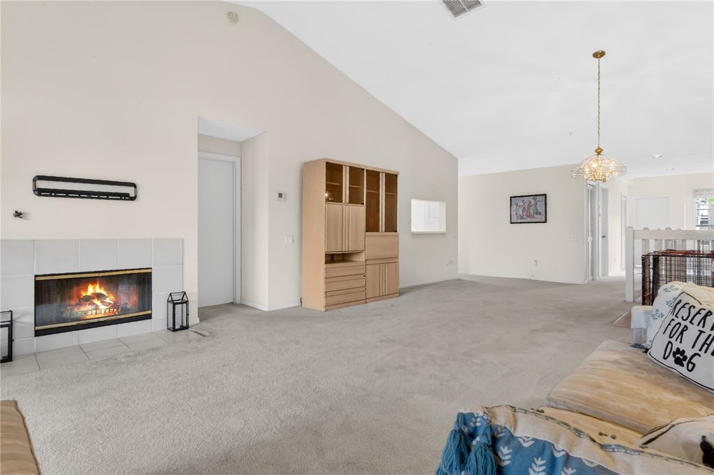 A living room features a fireplace, beige carpeting, a tall wooden cabinet, and vaulted ceilings — 6126 SUNNYVALE DRIVE UNIT 2303, ORLANDO, FL