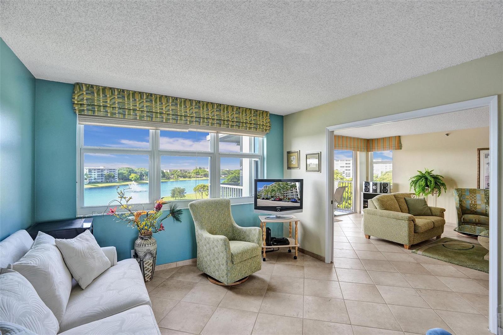 A living room with tile floors, a white sofa, and a view of a lake — 2900 N Course Drive # 602, Pompano Beach FL 33069, POMPANO BEACH, FL