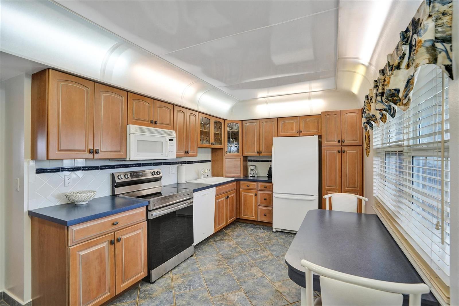 A kitchen with wood cabinets, blue countertops, stainless steel appliances, and a dining table — 2900 N Course Drive # 602, Pompano Beach FL 33069, POMPANO BEACH, FL
