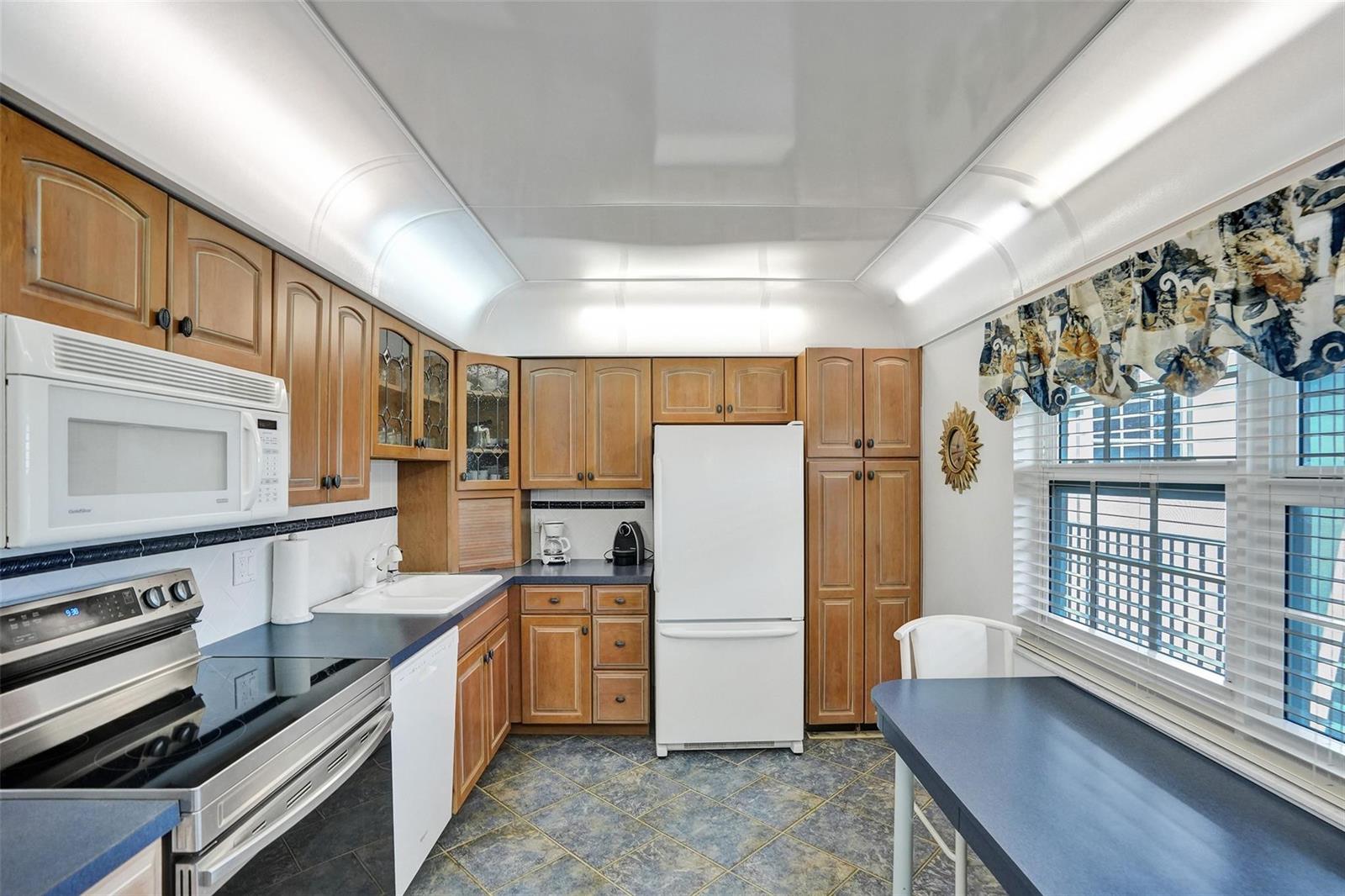 A kitchen features wood cabinets, blue countertops, a white refrigerator, and a built-in dining table — 2900 N Course Drive # 602, Pompano Beach FL 33069, POMPANO BEACH, FL