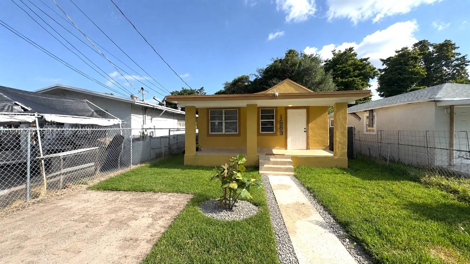 A yellow single-story house features a covered front porch, a walkway, and a chain-link fence — 1669 NW 70th St, Miami FL 33147, MIAMI, FL