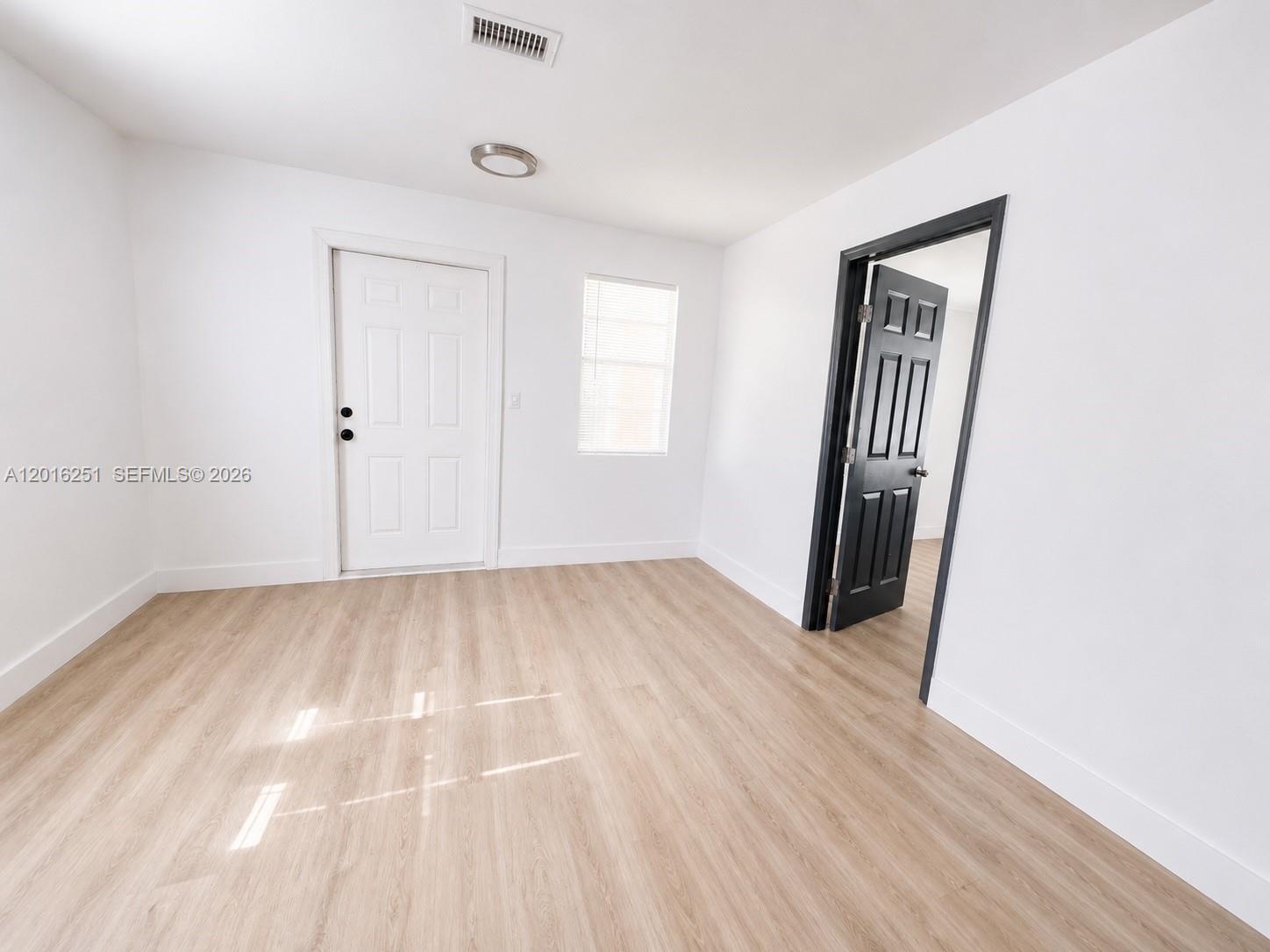A room with white walls, light wood-look flooring, a white door, and a black door — 1669 NW 70th St, Miami FL 33147, MIAMI, FL