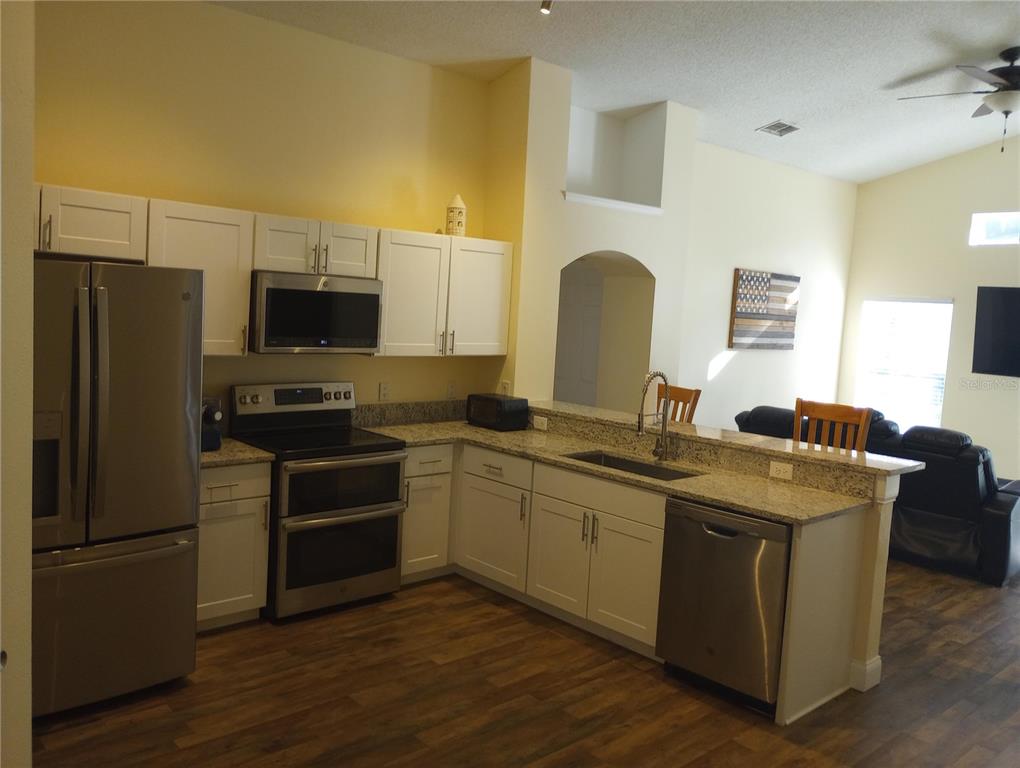 A kitchen features white cabinets, stainless steel appliances, granite countertops, and wood-look flooring — 7947 GOLDEN POND CIRCLE, KISSIMMEE, FL