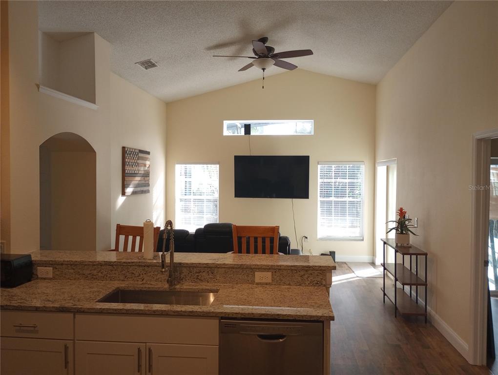 A kitchen island with granite countertops overlooks a living room with a vaulted ceiling — 7947 GOLDEN POND CIRCLE, KISSIMMEE, FL
