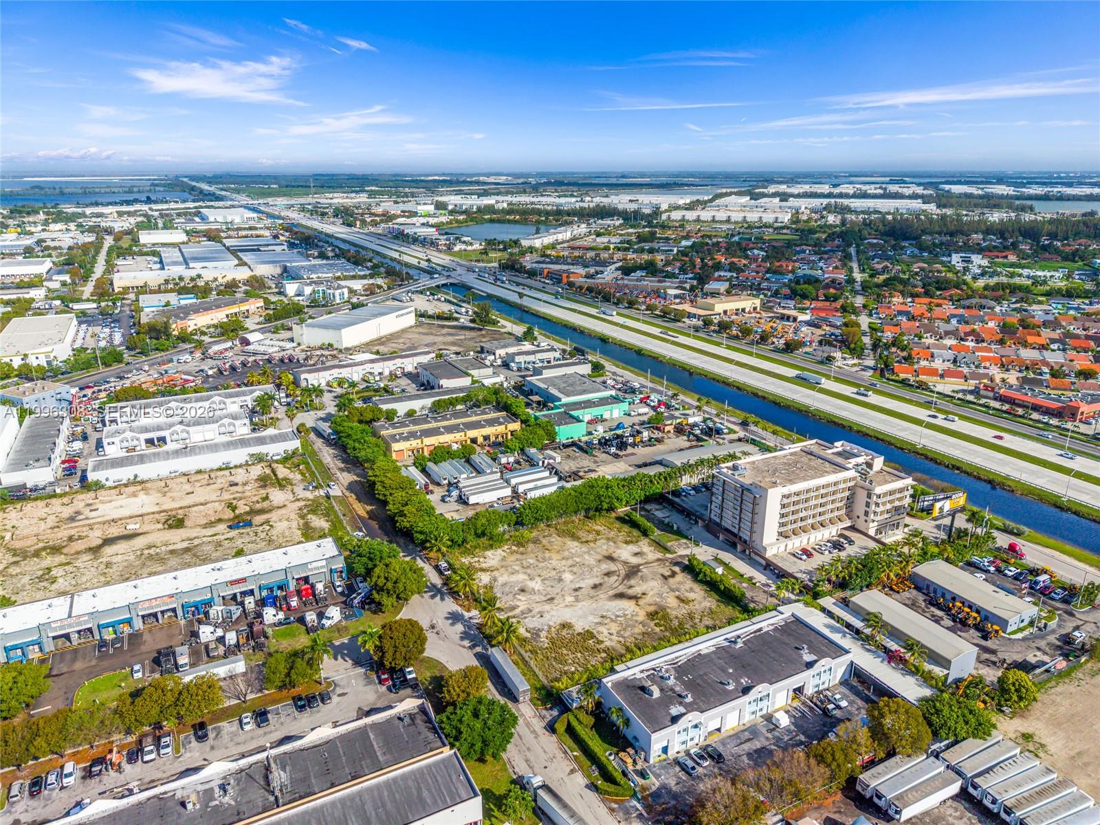 An aerial view shows industrial buildings, a vacant lot, and a highway beside a canal — 10633 NW 123rd St Rd, Medley FL 33178, MEDLEY, FL