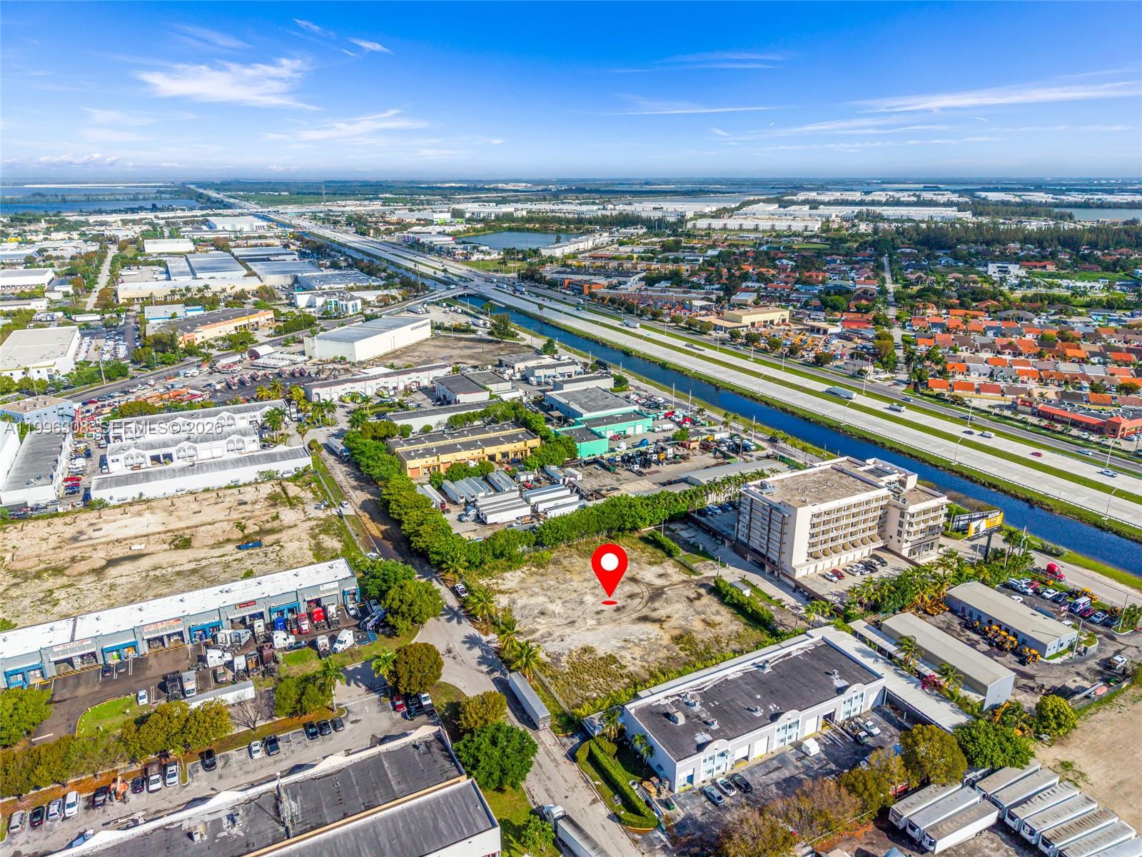 An aerial view shows a vacant, dirt-covered lot situated between industrial buildings and a highway — 10633 NW 123rd St Rd, Medley FL 33178, MEDLEY, FL