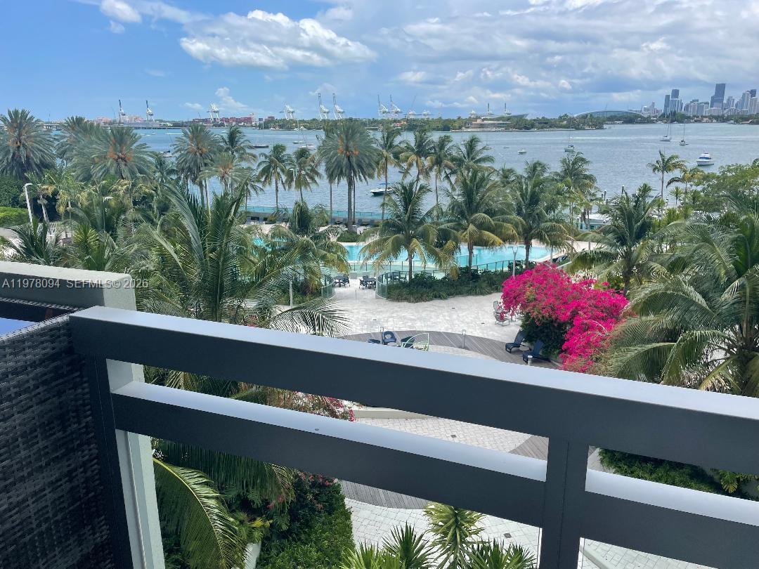 A balcony overlooks a swimming pool, palm trees, a bay, and a distant city skyline — 1500 Bay Rd # 524S, Miami Beach FL 33139, MIAMI BEACH, FL