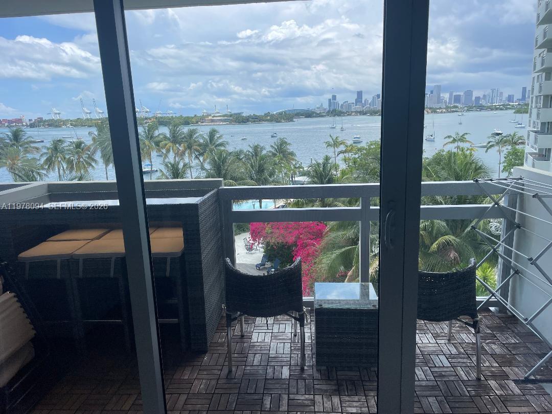 A balcony with outdoor furniture overlooks a bay, palm trees, and a distant city skyline — 1500 Bay Rd # 524S, Miami Beach FL 33139, MIAMI BEACH, FL