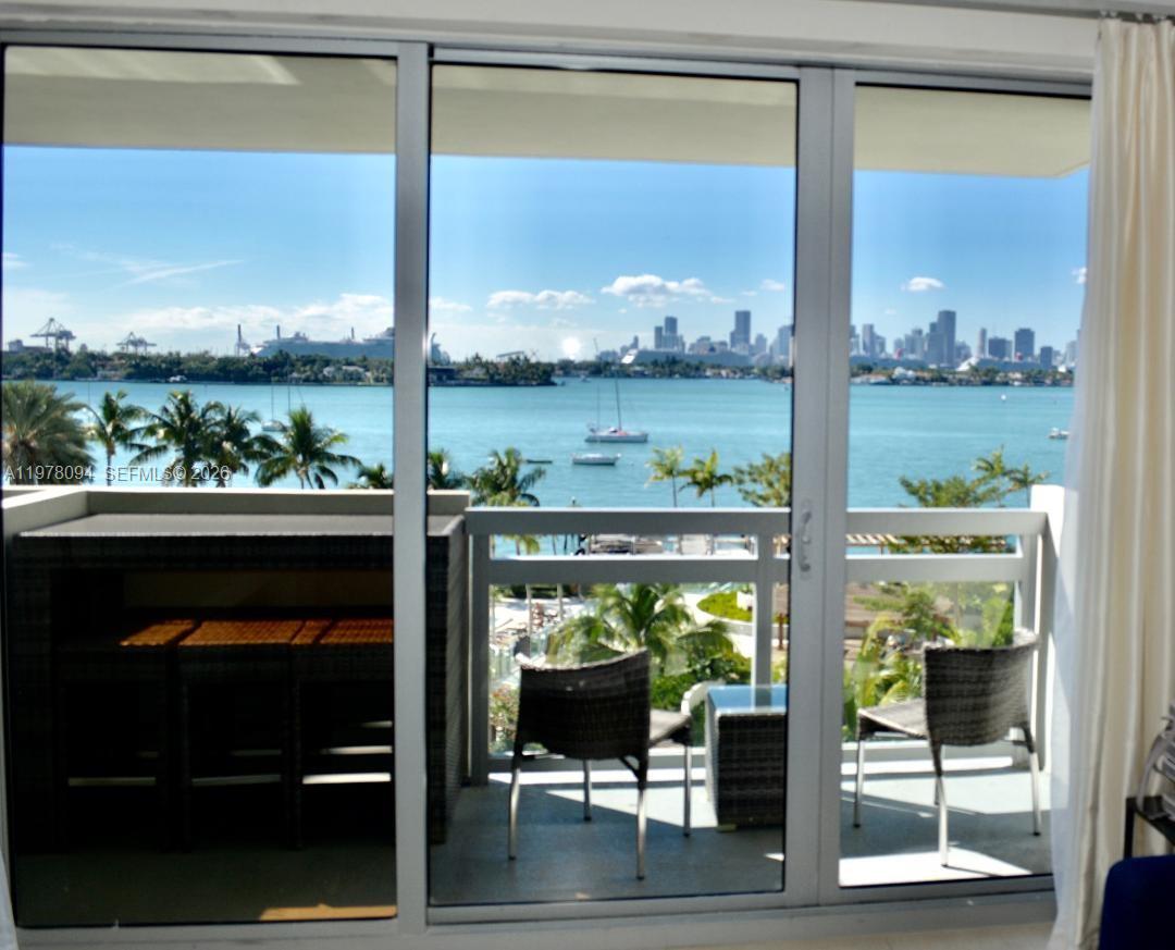 A balcony with outdoor furniture overlooks a bay with a city skyline in the distance — 1500 Bay Rd # 524S, Miami Beach FL 33139, MIAMI BEACH, FL