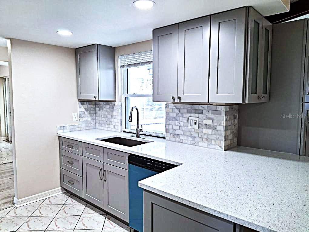 A kitchen features gray cabinets, white speckled countertops, a tiled backsplash, and a blue dishwasher — 8308 123RD AVENUE, LARGO, FL