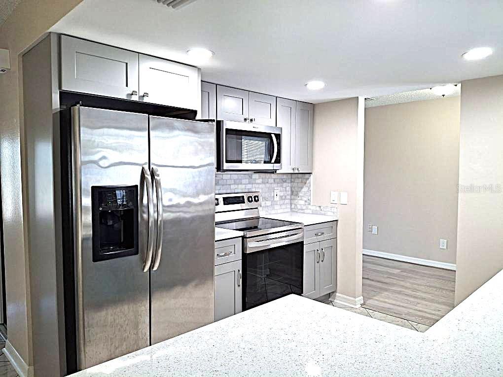A kitchen features stainless steel appliances, light gray cabinets, and white speckled countertops — 8308 123RD AVENUE, LARGO, FL
