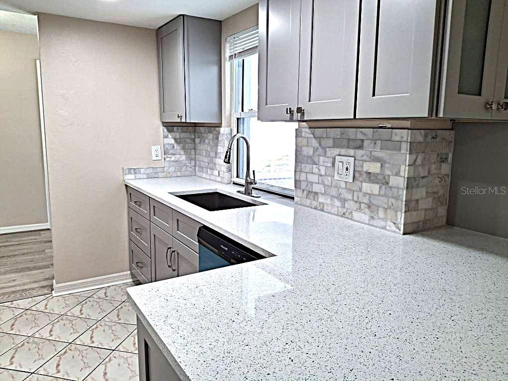 A kitchen features gray cabinets, white speckled countertops, and a marble tile backsplash — 8308 123RD AVENUE, LARGO, FL