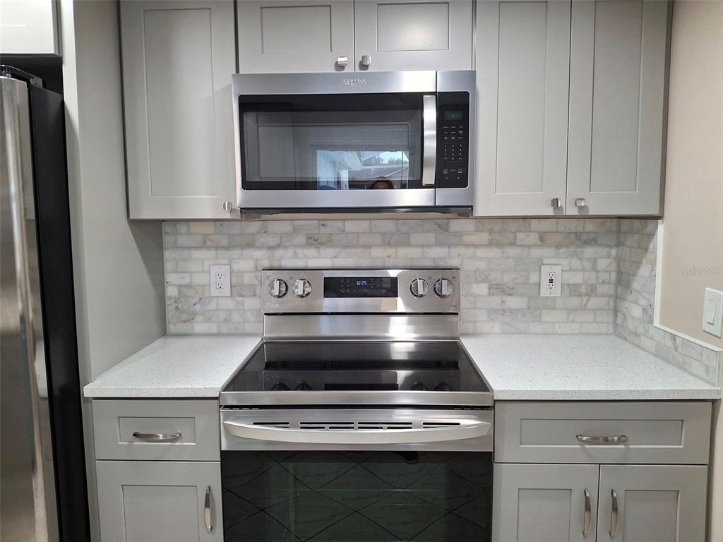 A kitchen features gray cabinets, a stainless steel microwave and stove, and a marble backsplash — 8308 123RD AVENUE, LARGO, FL