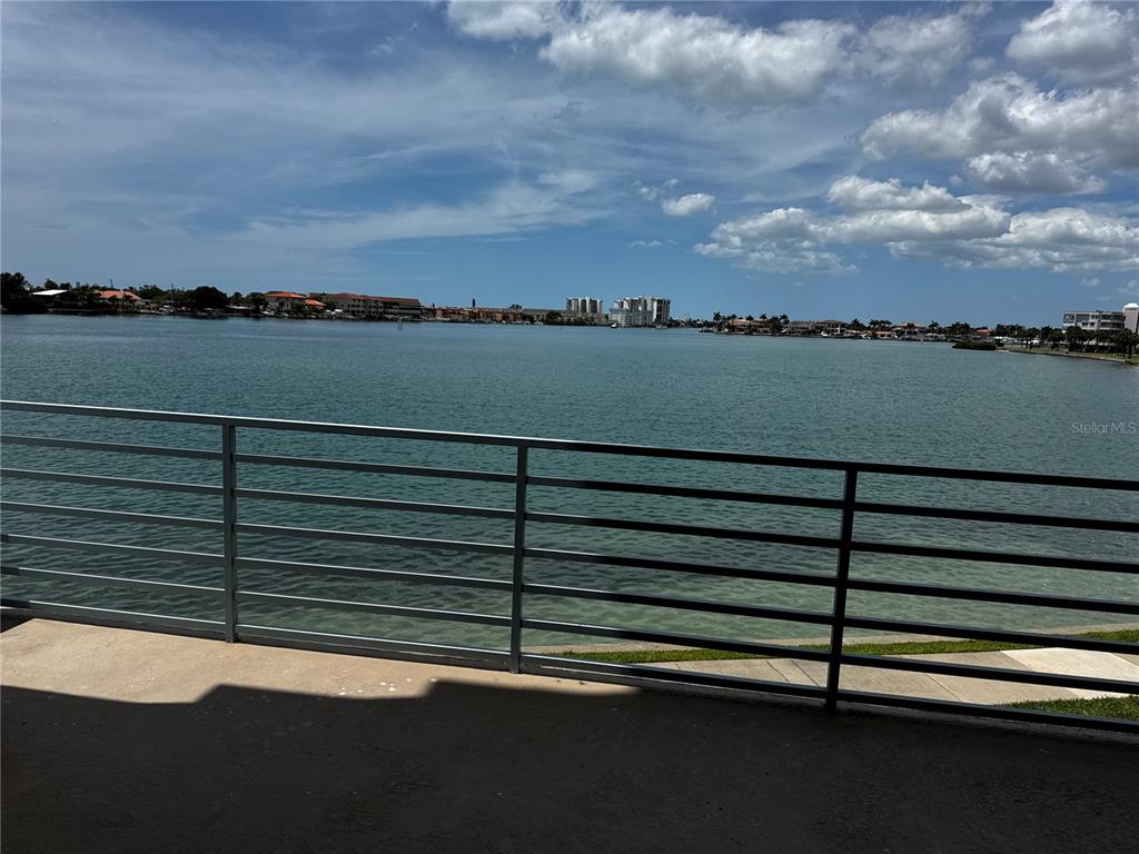 A metal balcony railing overlooks a wide bay with distant buildings under a cloudy sky — 7932 SAILBOAT KEY BOULEVARD S UNIT 101, SOUTH PASADENA, FL