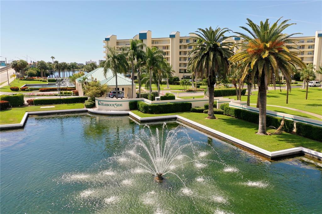 An aerial view shows a fountain in a pond before a multi-story apartment building — 7932 SAILBOAT KEY BOULEVARD S UNIT 101, SOUTH PASADENA, FL