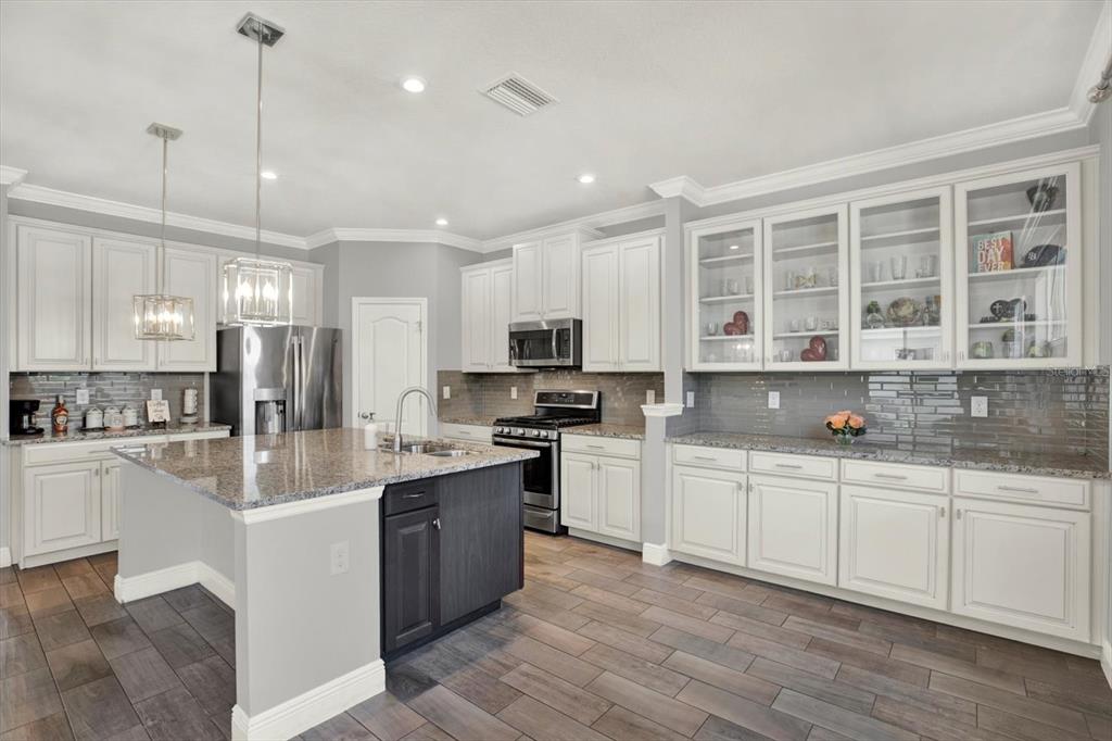 A modern kitchen features white cabinets, a dark island, granite countertops, and wood-look tile flooring — 11702 LAKE LUCAYA DRIVE, RIVERVIEW, FL