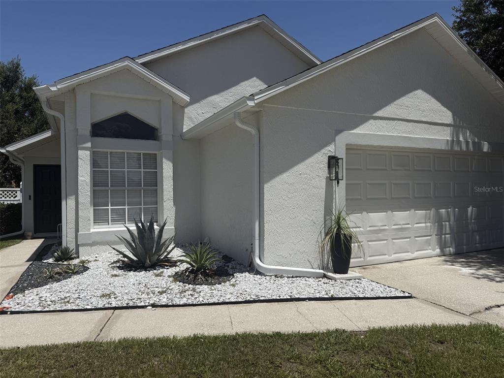 A white stucco house features a two-car garage, a front window, and a rock garden — 2916 CANOE CIRCLE, ST CLOUD, FL