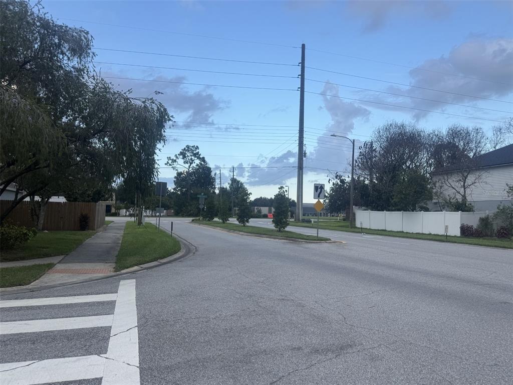 A view of a paved suburban street with a crosswalk, trees, and utility poles — 2916 CANOE CIRCLE, ST CLOUD, FL