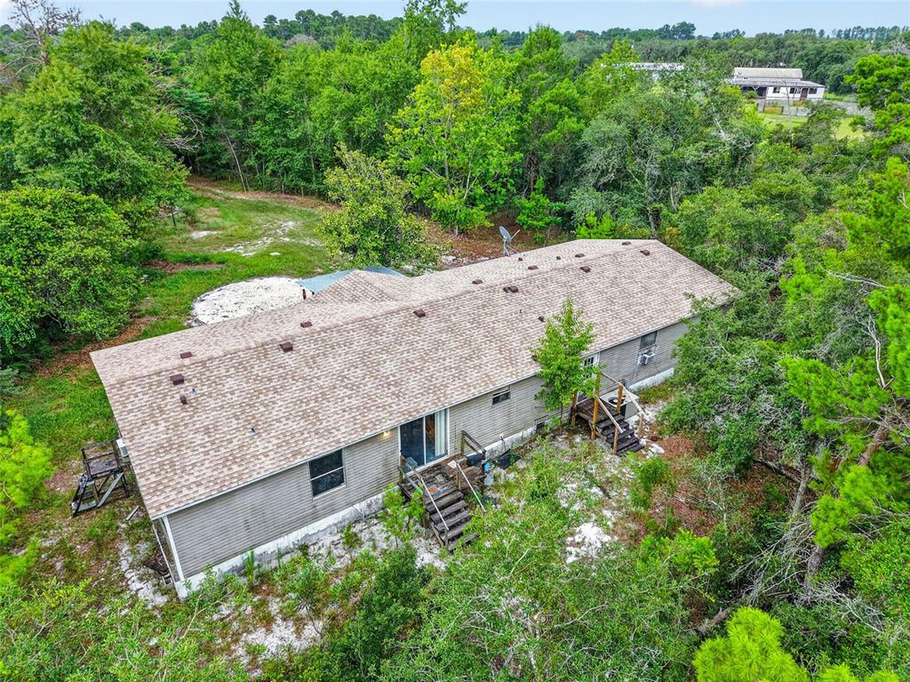 An aerial view shows a single-story house with a shingled roof surrounded by dense trees — 20241 SALTSDALE ROAD, UMATILLA, FL