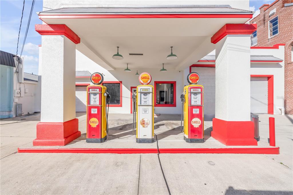 Three vintage Shell gas pumps stand under a covered canopy in front of a building — 208 MAGNOLIA ST, NEW SMYRNA BEACH, FL