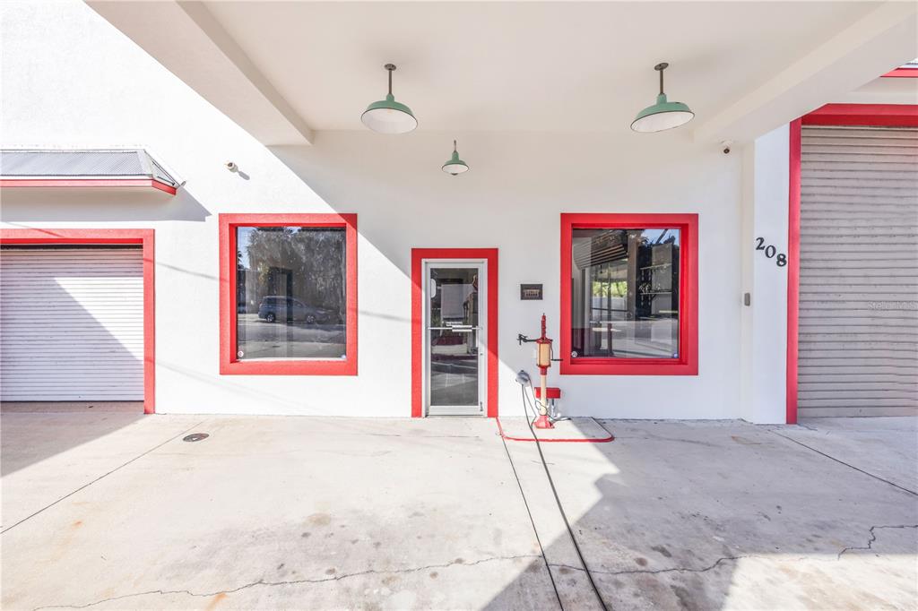 The exterior of a commercial building features a central glass door, two windows, and two roll-up doors — 208 MAGNOLIA ST, NEW SMYRNA BEACH, FL