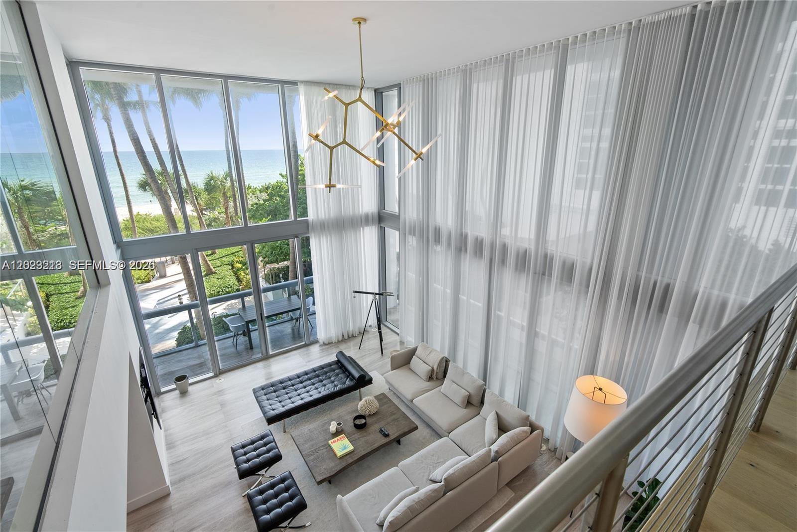 A high-ceilinged living room features floor-to-ceiling windows with ocean views and modern furniture — 6899 Collins Ave # 202, Miami Beach FL 33141, MIAMI BEACH, FL